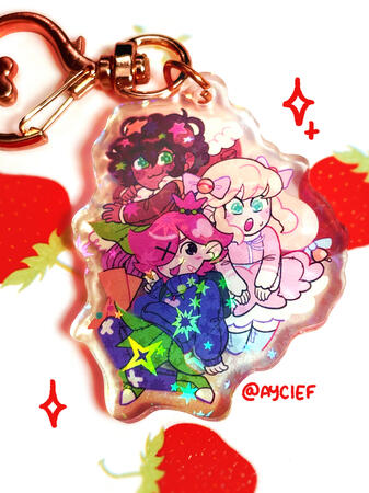 A keychain of Molly, Phoenica, and Trixie from Epithet Erased all posed with each other. It has a sparkly star holo finish.